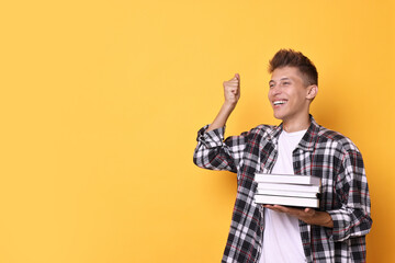 Young student with stack of books happy about his good exam result on yellow background, space for text