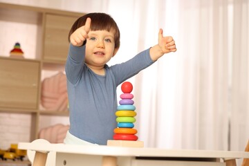 Cute little boy showing thumbs up at home