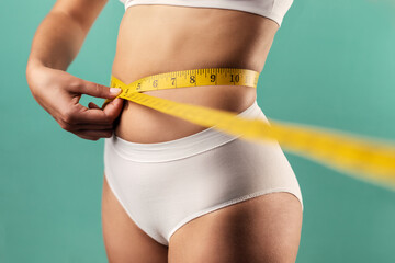 Woman measuring her slim body. Isolated on blue background