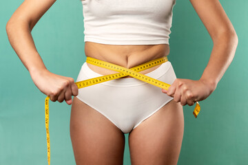 Woman measuring her slim body. Isolated on blue background