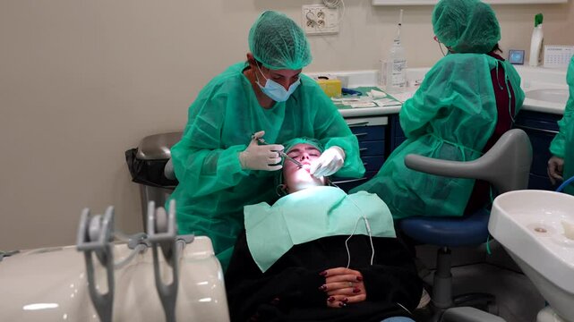 Dentist applies anesthesia in clinic with assistants checking records nearby