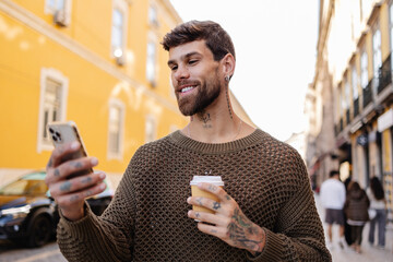 Smiling tourist using smartphone and holding coffee in lisbon, portugal