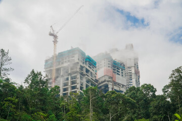 Buildings under construction and clouds above them with trees. a building being built on top of the mountain with fog around it and a crane on top of it. building construction concept with copy space