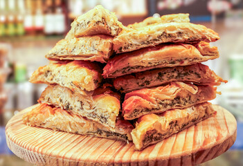 This image shows a stack of freshly baked Spanish empanadas, featuring layers of flaky pastry filled with meats, cheeses, and vegetables, displayed on a wooden board.