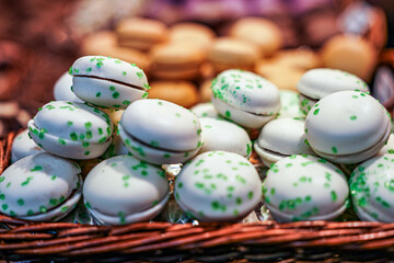 Delightful assortment of white chocolate macarons sprinkled with vibrant green sugar crystals, artistically presented in a basket, perfect for festive occasions