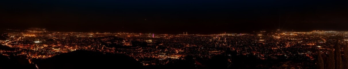 A panoramic night view of Barcelona from the Church of the Sacred Heart on Tibidabo Mountain, showcasing the vibrant city lights spread across the landscape.