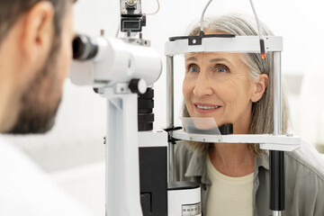 Senior woman undergoing eye exam with slit lamp by optometrist