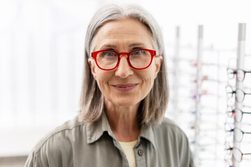 Beautiful, smiling senior woman smiling wearing red eyeglasses in optical store