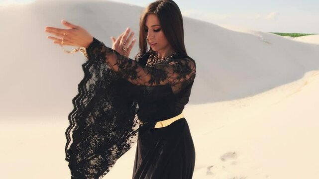 happy woman dancing in desert. Long black silk dress and hair flying fluttering in wind slow motion. Fashion model posing. Girl tourist is enjoying vacation in Dubai desert summer nature. Video 4k