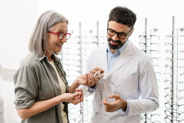 Senior woman choosing eyeglasses with optician's help in optical store