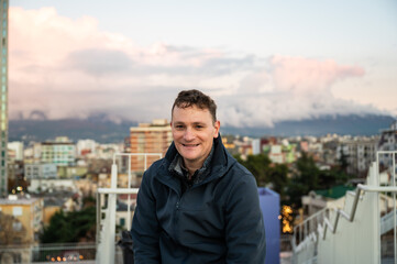 Portrait  of a 45 yo man with the city of Tirana at dusk in the background, Albania