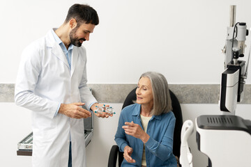Optometrist showing phoropter to senior woman in ophthalmology clinic