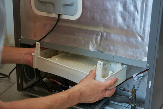man takes Compressor tray with water from refrigerator, defrosting refrigerator, tray for collecting melted water in refrigerator