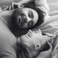Monochrome bw portrait image - young couple looking at each other, lay on bed. Blond hair woman...