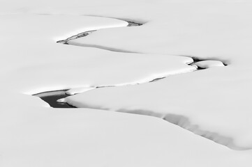 A small brook flows through a snow-covered plain
