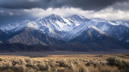 Dramatic snow-capped mountain range under a stormy sky, overlooking a vast, dry plain.