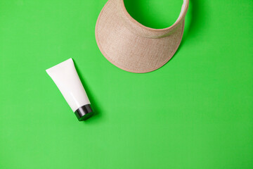 White sunscreen bottle with visor on green background. Sunscreen concept. Travel concept. space for text.