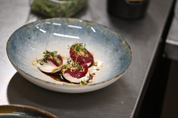A close-up shot of a vibrant vegetarian dish, featuring marinated slices of red beetroot, goat cheese, and nuts, served as an appetizer on a plate