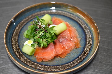 A close-up shot of a traditional dish featuring smoked salmon, a colorful appetizer with a dressing and a fresh cucumber salad.