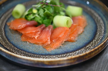A close-up shot of a traditional dish featuring smoked salmon, a colorful appetizer with a dressing and a fresh cucumber salad.