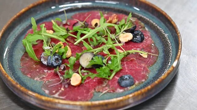 Beef carpaccio with arugula and blueberries on a wooden table, closeup video