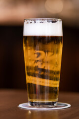 A frothy glass of golden beer sits on a rustic wooden table, capturing the essence of relaxation, refreshment, and timeless enjoyment in a cozy setting.