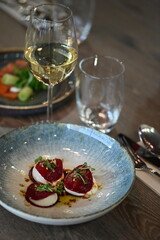 A close-up shot of a beautifully plated appetizer served in a rustic restaurant setting. The dish features marinated red beetroot paired with creamy goat cheese, garnished with fresh herbs.