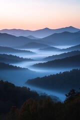 Obraz premium Layers of foggy blue mountains in the distance under a pale dawn sky.