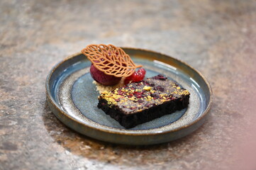 A view of a chocolate dessert on a rustic plate, featuring a sorbet and a cookie, served as a...