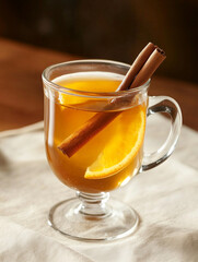 Warm mulled wine in a glass mug, garnished with cinnamon stick and orange slice, cozy winter setting 