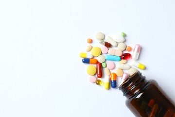 Various pills pouring out of medicine bottle on white background