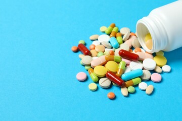 Various pills pouring out of medicine bottle on color background