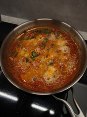 Aromatic tomato sauce cooking in a pan, topped with grated cheese and herbs, creating a flavorful and comforting dish