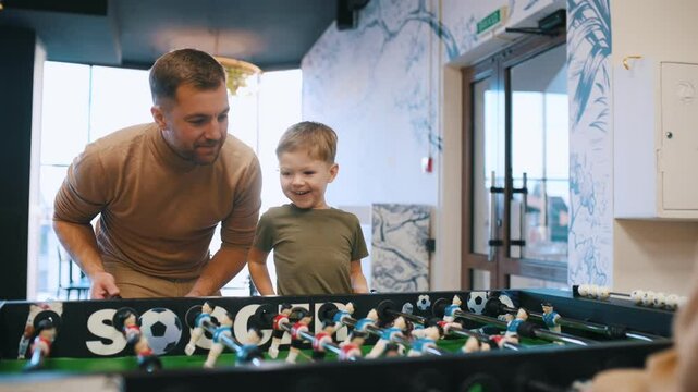Conception of entertainment. Father and son are playing table football game indoors.