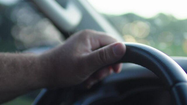 Close up of unknown male drive camper van or delivery truck on winding mountain road between the trees near green forest at sunny day. Man drives car, hold hands on steering wheel. Slow motion
