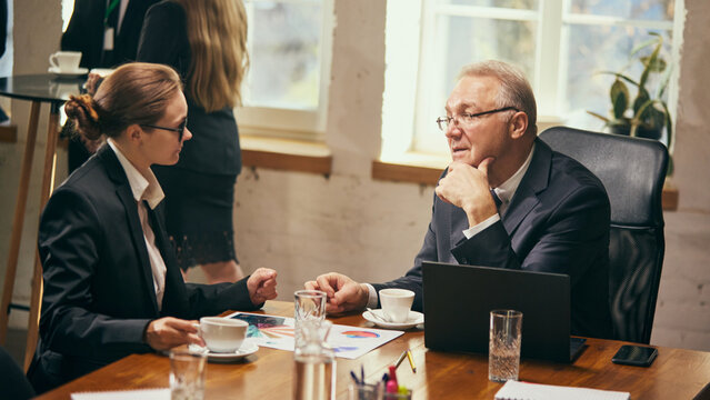 Senior businessman sitting at table and talking to a young female employee, sharing knowledges, career advice and guidance. One-on-one conversation. Business, mentorship, personal consultation concept