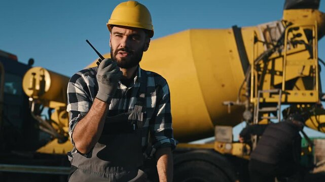 Man is standing against concrete mixer truck. Worker is on the construction site at daytime.