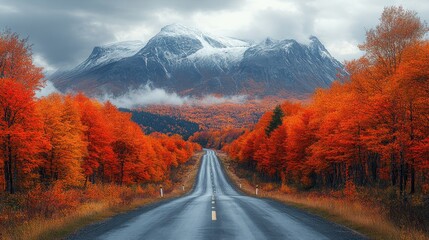 Scenic autumn road through vibrant red forest towards snow-capped mountains under a cloudy sky.