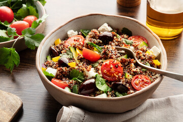 Quinoa salad, healthy Mediterranean lunch with fresh organic vegetables, cheese, and olives, on a rustic wooden table