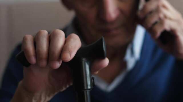 elderly man 75 years old talking on phone sitting holding walking stick with hand real pensioner everyday life