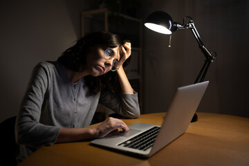 Tired woman working late at night using laptop at home office.