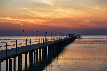 Fototapeta premium Beautiful sunrise on Red Sea, Marsa Alam, Egypt, outline of the boat, umbrellas, beach, chillout in the morning. Silhouettes of people against the background of sunrise, A jetty extending into the sea