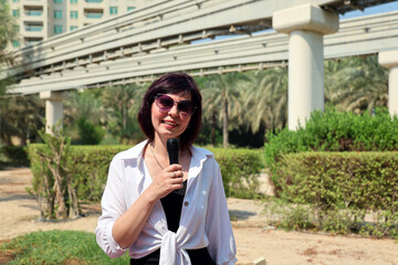 A TV news reporter in the city near an aerial railway monorail.