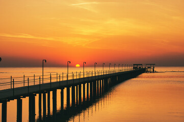 Obraz premium Beautiful sunrise on Red Sea, Marsa Alam, Egypt, outline of the boat, umbrellas, beach, chillout in the morning. Silhouettes of people against the background of sunrise, A jetty extending into the sea