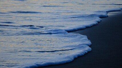 The soft hues of the setting sun reflect off the gentle, quiet waves, creating an atmosphere of peace and intimacy. 