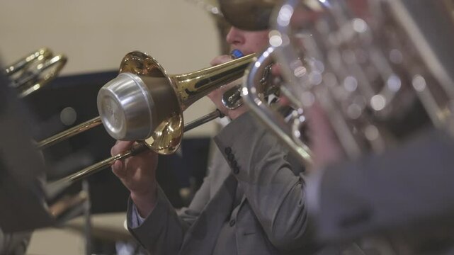 A musician playing a trombone with a straight mute during a wind band concert