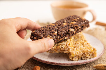 Granola bars with caramel, nuts, flakes in ceramic plate with hand on white wooden. Side view, selective focus.