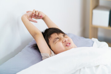 Asian boy wakes up in the early morning, feeling groggy and reluctant to leave the comfort of his bed. 