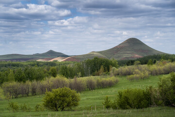 Fototapeta premium A valley covered with trees and bushes against a backdrop of low mountains. The sun breaks through the clouds.