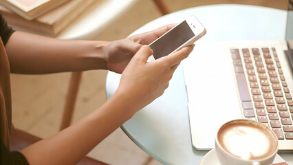 Hands Holding Smartphone Next to Laptop in Casual Workspace